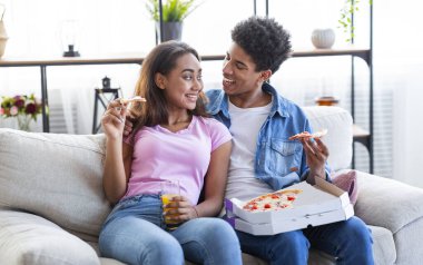 Neşeli genç çift TV karşısında pizza yiyorlar.