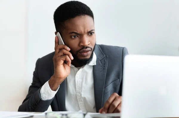 Serieuze zakenman praten over de telefoon en met behulp van laptop in het kantoor — Stockfoto