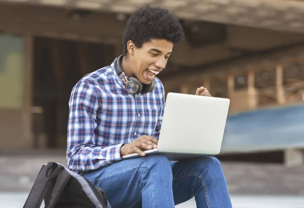 Podekscytowany młody facet obchodzi zwycięstwo z laptopem na zewnątrz — Zdjęcie stockowe