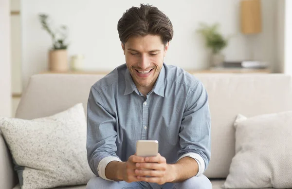 Happy Guy Przeglądanie na Smatphone siedzi na kanapie w domu — Zdjęcie stockowe
