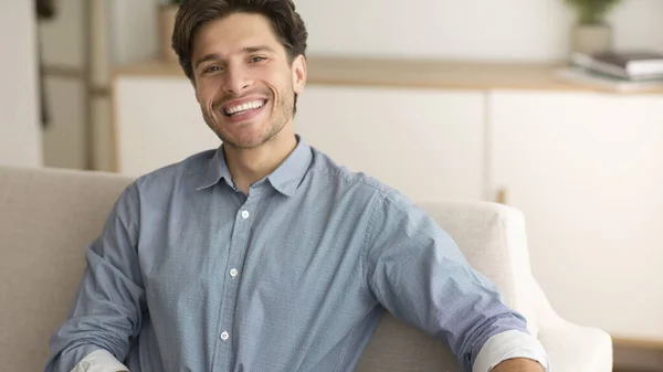 Alegre chico sonriendo en cámara descansando en sofá en casa —  Fotos de Stock