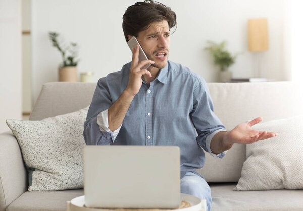 Unsatisfied Guy Complaining About Problems With Laptop By Phone Indoor