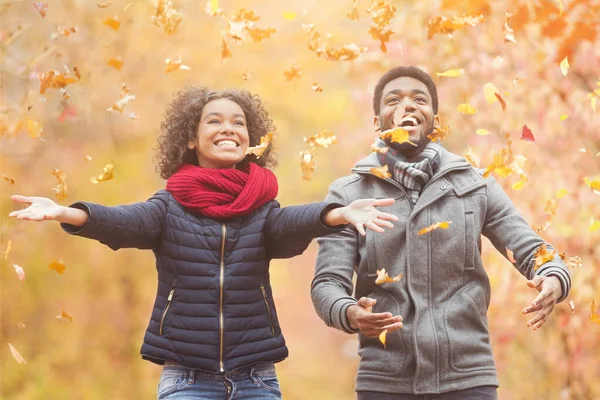 Feliz afro pareja lanzando otoño otoño hojas —  Fotos de Stock