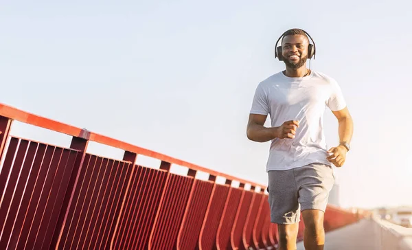 Šťastný černoch běží po mostě, poslouchá hudbu — Stock fotografie