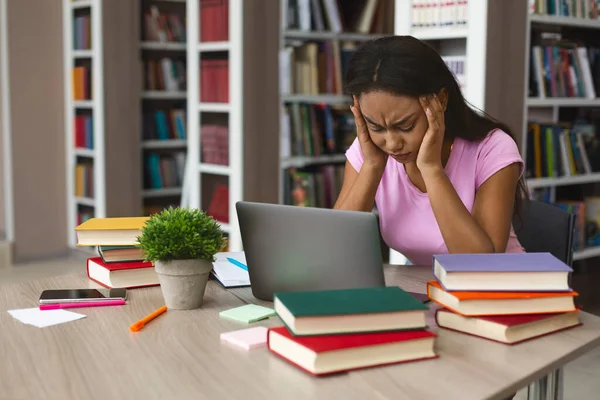 Stanco afro ragazza bloccato con computer portatile e libri in biblioteca — Foto Stock