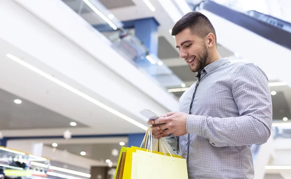 Przystojny mężczyzna korzystający z telefonu, robi zakupy w centrum handlowym — Zdjęcie stockowe