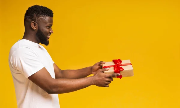 Smiling african guy with gift box over yellow studio background
