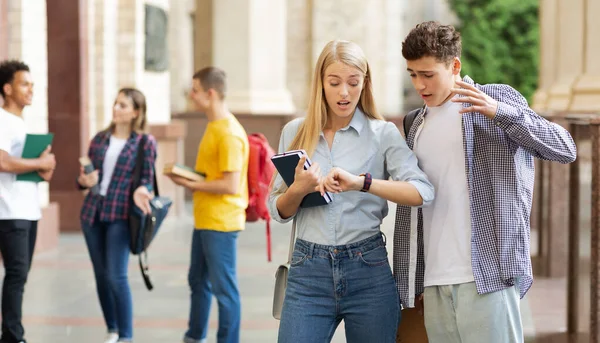 Studenci w kampusie uniwersyteckim patrzą na zegarki — Zdjęcie stockowe