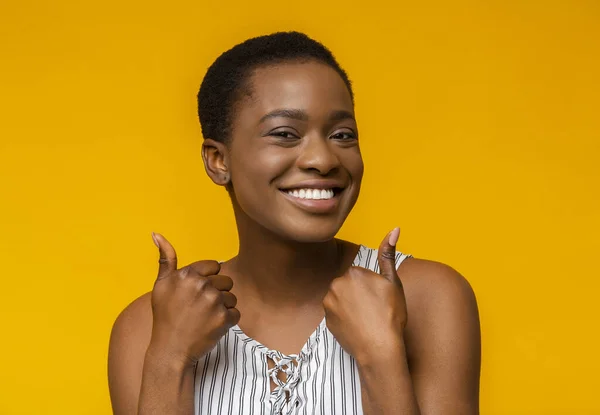 Overblij afro meisje tonen duimen omhoog op gele achtergrond — Stockfoto