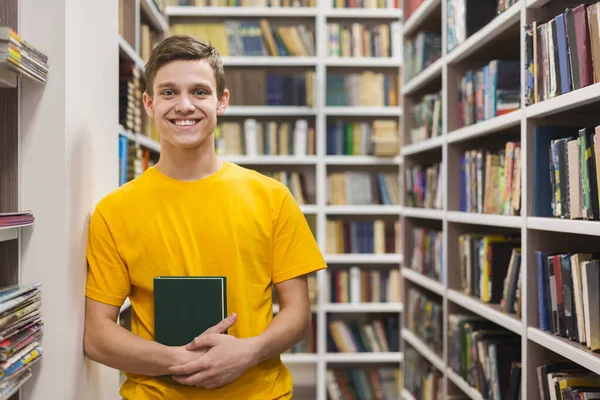 Wesoły uczeń stojący między regałami w bibliotece — Zdjęcie stockowe