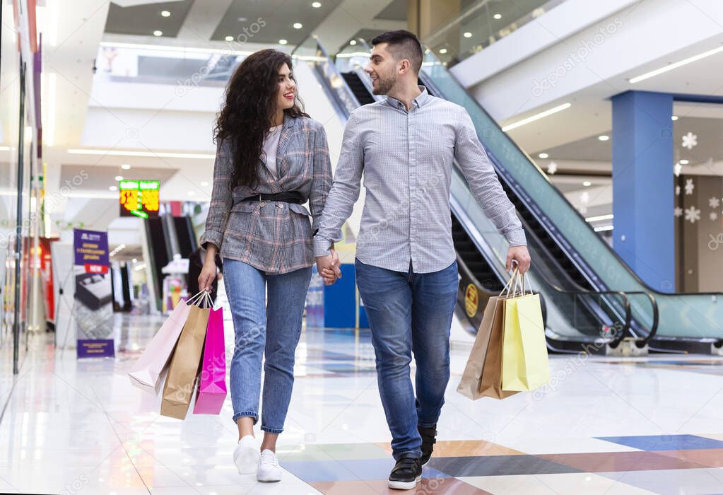 Happy millennial couple walking after shopping in mall