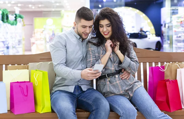 Ευτυχισμένο ζευγάρι που ξεκουράζεται στο εμπορικό κέντρο στον πάγκο, χρησιμοποιώντας το τηλέφωνο — Φωτογραφία Αρχείου