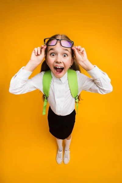 Überglückliches Schulmädchen mit Brille posiert auf gelbem Hintergrund — Stockfoto