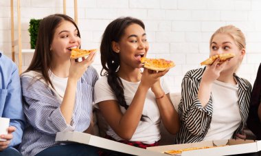 Atıştırma zamanı. Mutlu kızlar pizza yiyip sohbet ediyorlar.