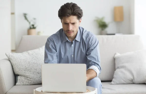 Uomo che lavora al computer portatile seduto sul divano a casa — Foto Stock