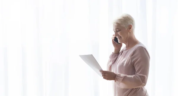 Alte Frau hält Dokumente in der Hand und telefoniert mit Kunden — Stockfoto