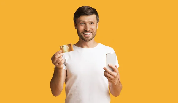 Guy Holding Credit Card And Smartphone, Yellow Background — Stockfoto