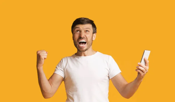 Emotional Man Shouting Holding Smartphone Shaking Fists, Yellow Background — Stok Foto