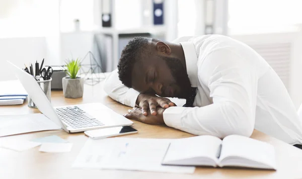 Uitgeputte Afrikaanse werknemer die op zijn werkplek slaapt — Stockfoto