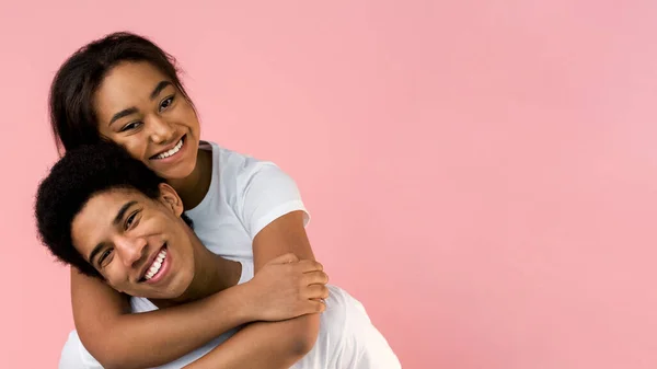 Cara feliz carregando sua namorada nas costas, fundo rosa — Fotografia de Stock