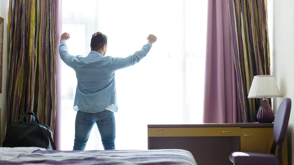 Hombre estirándose frente a la ventana en la habitación de hotel —  Fotos de Stock