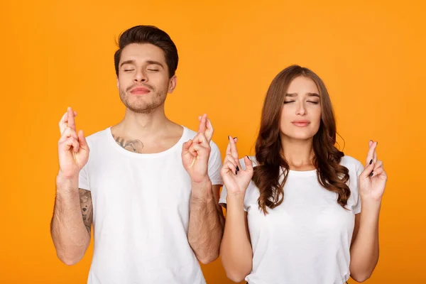 Joven hombre y mujer cerrando sus ojos y cruzando los dedos — Foto de Stock