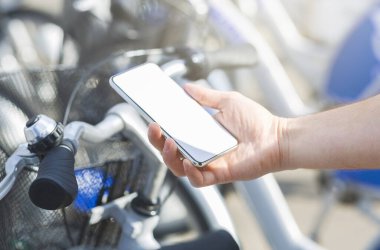 Man with cellphone renting bike at city sharing station outdoors