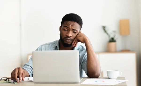 Uttråkad svart arbetare tittar på bärbar skärm, kan inte koncentrera — Stockfoto