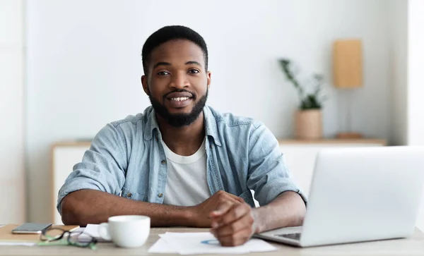 Leende afrikansk amerikansk arbetare tittar på kameran, sitter på arbetsplatsen — Stockfoto