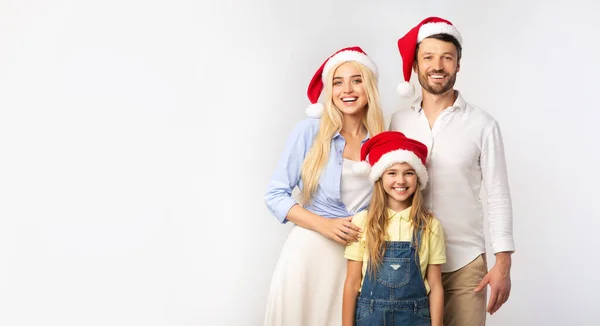 Family Of Three In Christmas Santa Hats Standing In Studio