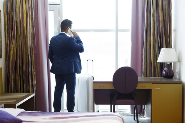 Empresário chamando o serviço de táxi do quarto de hotel, ficando perto da janela — Fotografia de Stock