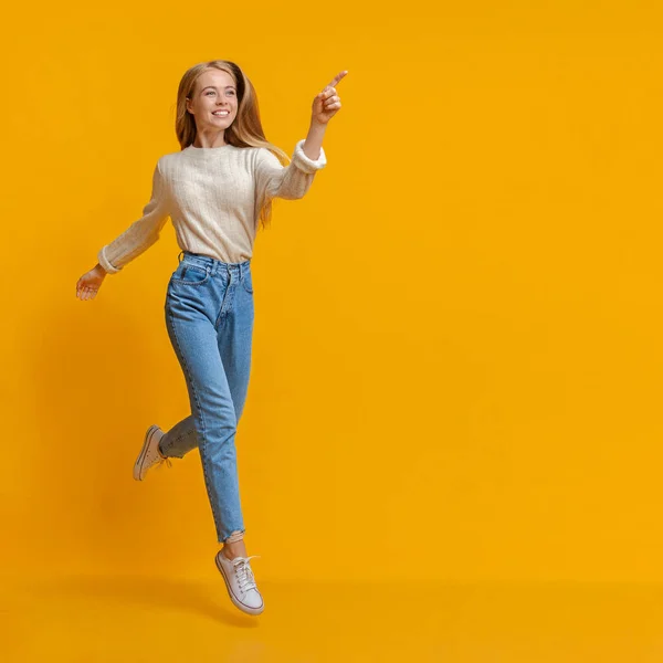 Glada tonåring flicka hoppar och pekar åt sidan på orange bakgrund — Stockfoto