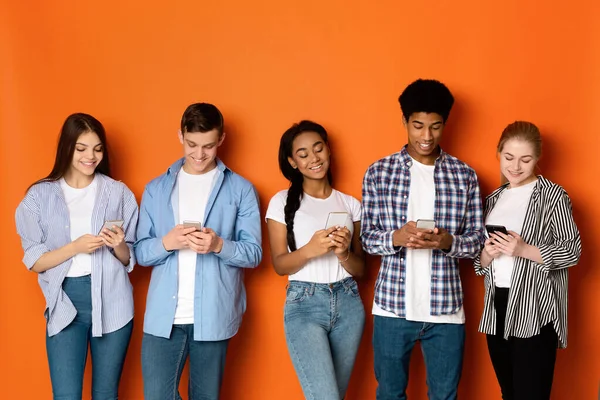 Gadget addiction. College friends with smartphones, orange wall