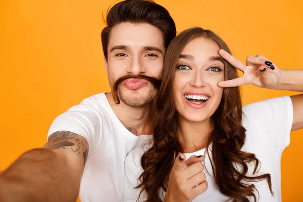 Casal tirando selfie, mulher mostrando símbolo de paz perto de seu olho — Fotografia de Stock