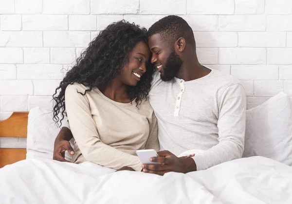 Casal abraçando na cama tocando as testas e usando o smartphone juntos — Fotografia de Stock