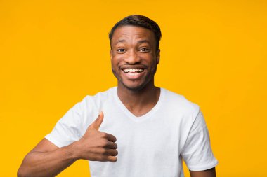 Afro Adam Başparmağıyla hareket ediyor Kameraya gülümsüyor, Sarı Arkaplan