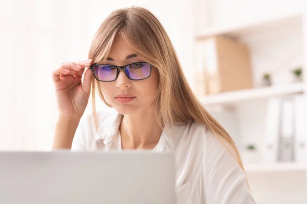 Empresária olhando através dos óculos no laptop sentado no escritório — Fotografia de Stock
