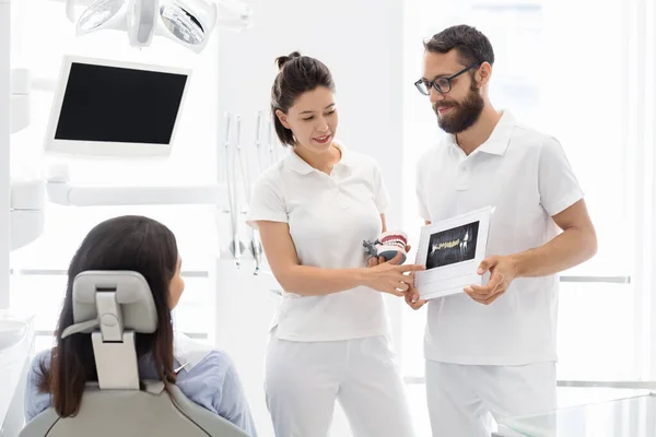 Due dentisti che mostrano e spiegano il trattamento della malattia dei denti al paziente — Foto Stock