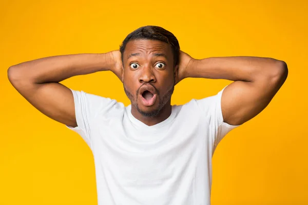 Shocked afro hombre embrague cabeza de pie sobre amarillo estudio fondo — Foto de Stock