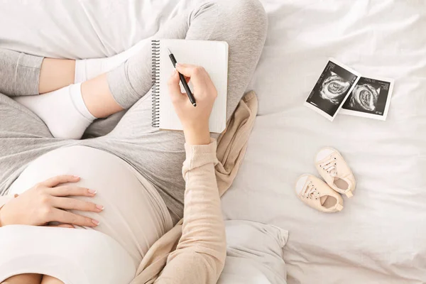 Mujer embarazada preparándose para el parto, sentada en la cama con cuaderno —  Fotos de Stock