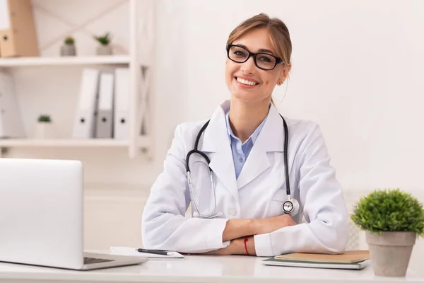 Nainen lääkäri hymyilee kamerassa istuu moderni klinikka toimisto — kuvapankkivalokuva