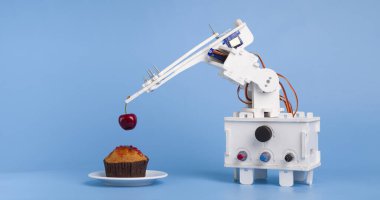 Robot tatlı pişiriyor, tatlı keki taze kirazla süslüyor.