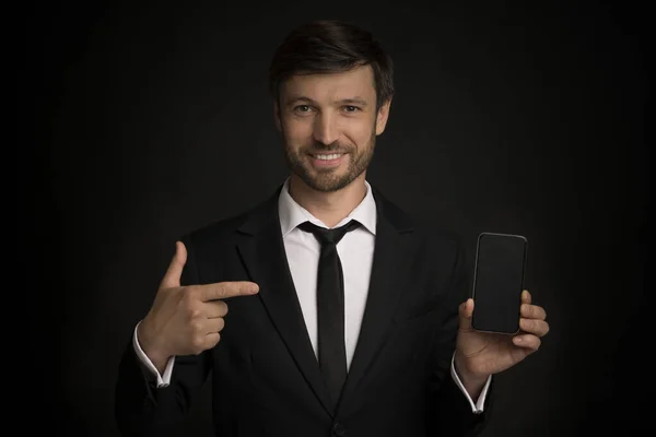 Geschäftsmann zeigt mit dem Finger auf leeren Telefonbildschirm, schwarzer Hintergrund, Attrappe — Stockfoto