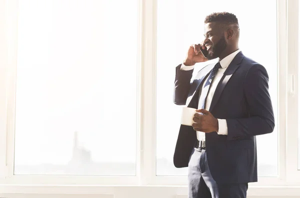 Привабливий бізнесмен розмовляє по телефону і п'є каву біля вікна — стокове фото