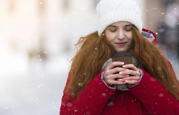 Chica con los ojos cerrados sosteniendo bebida caliente sobre fondo de invierno —  Fotos de Stock