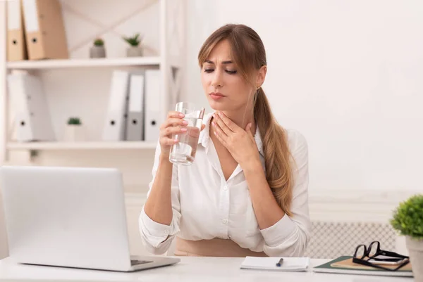 Señora que tiene dolor de garganta sosteniendo el vidrio de agua trabajando en la oficina —  Fotos de Stock