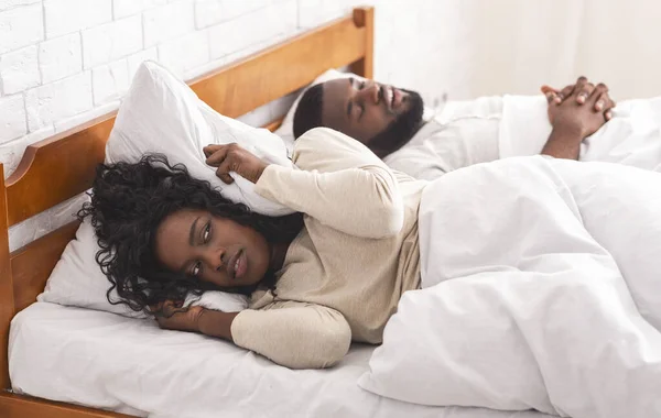 Чорна жінка, яка страждає хропінням хлопця, закриває вуха подушкою . — стокове фото