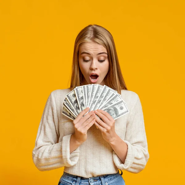 Şok olmuş genç bir kız elinde dolar banknotları tutuyor. — Stok fotoğraf