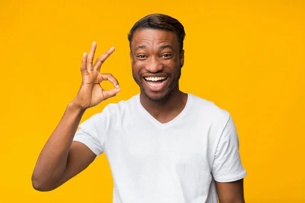 Podekscytowany czarny człowiek Gesturing Ok stojąc na żółty Studio tle — Zdjęcie stockowe
