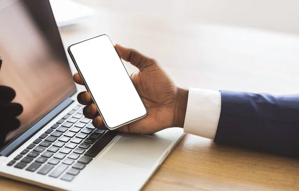 Empresario sosteniendo teléfono inteligente con pantalla en blanco y trabajando en el ordenador portátil — Foto de Stock